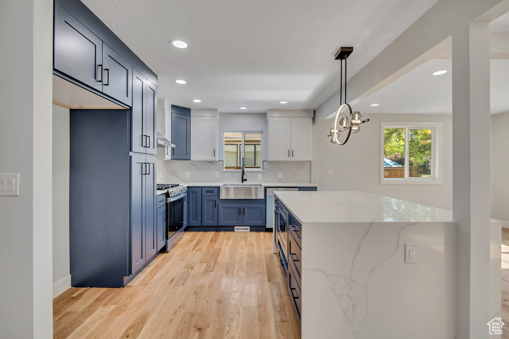 Kitchen with stainless steel range with gas stovetop, light wood-style flooring, backsplash, light stone counters, and recessed lighting