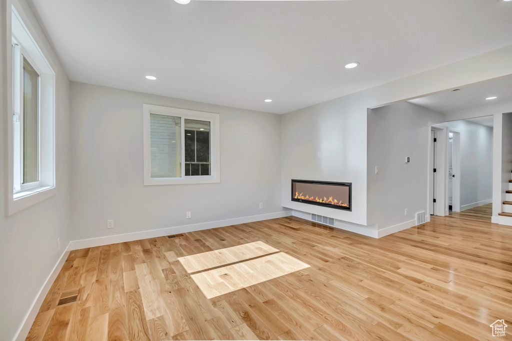 Unfurnished living room with light wood-style flooring, a glass covered fireplace, and recessed lighting
