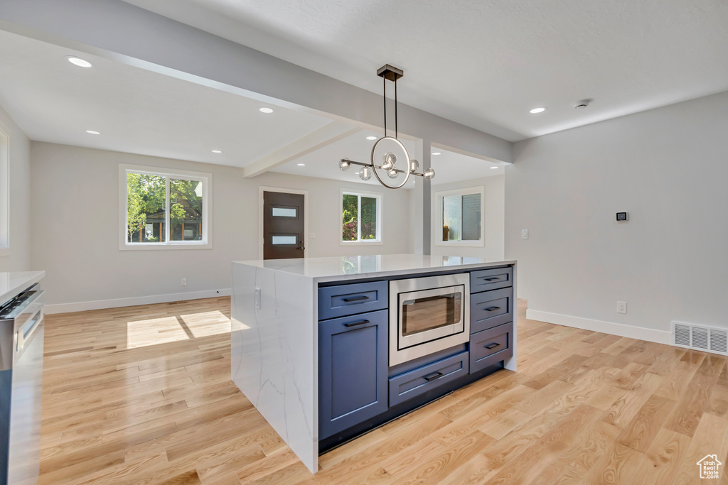 Kitchen featuring appliances with stainless steel finishes, light wood finished floors, healthy amount of natural light, recessed lighting, and beam ceiling