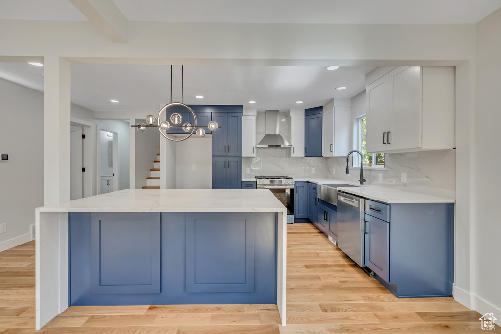 Kitchen with appliances with stainless steel finishes, wall chimney exhaust hood, a center island, tasteful backsplash, and blue cabinetry