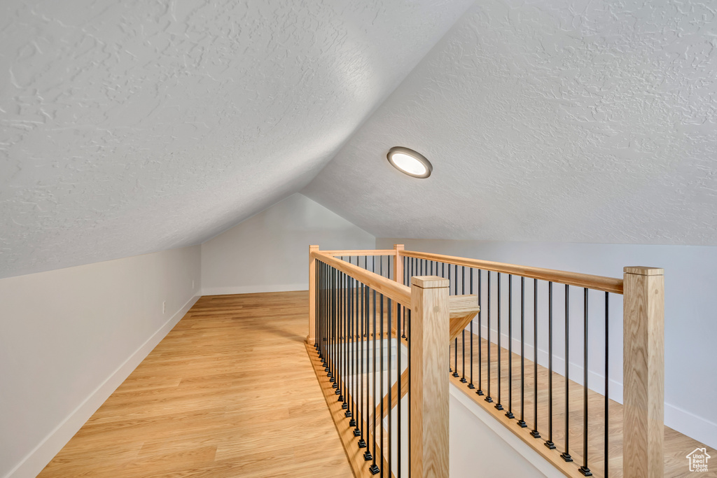 Hallway with a textured ceiling, an upstairs landing, vaulted ceiling, wood finished floors, and recessed lighting