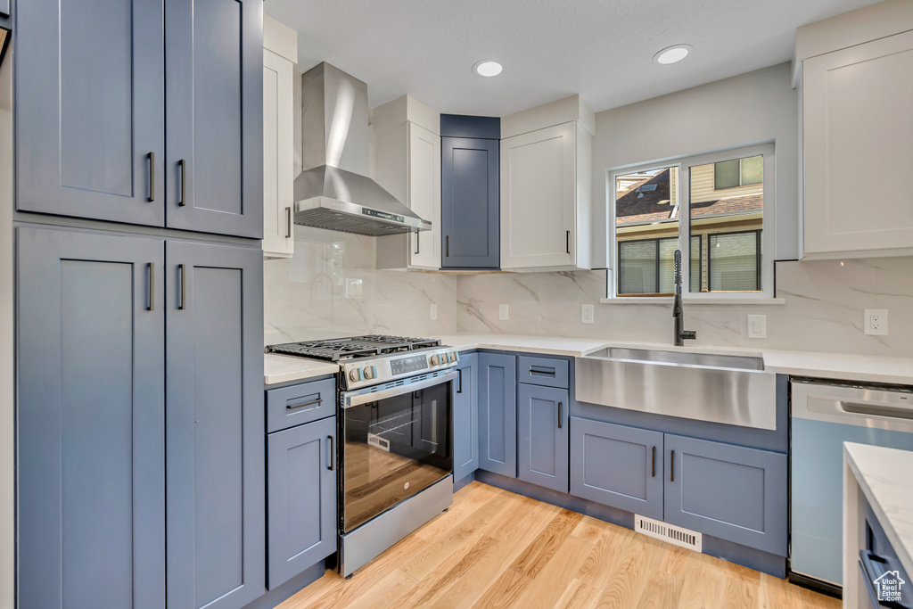 Kitchen with wall chimney range hood, stainless steel appliances, light countertops, decorative backsplash, and recessed lighting