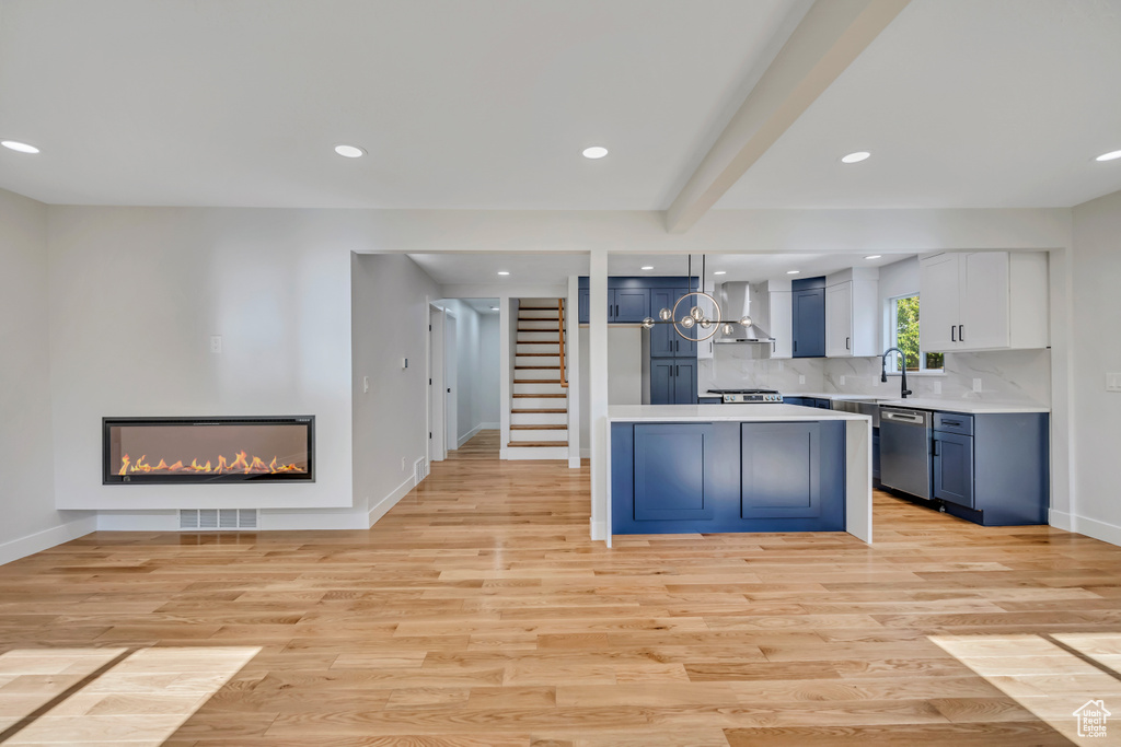 Kitchen with wall chimney range hood, dishwasher, a glass covered fireplace, light countertops, and blue cabinetry