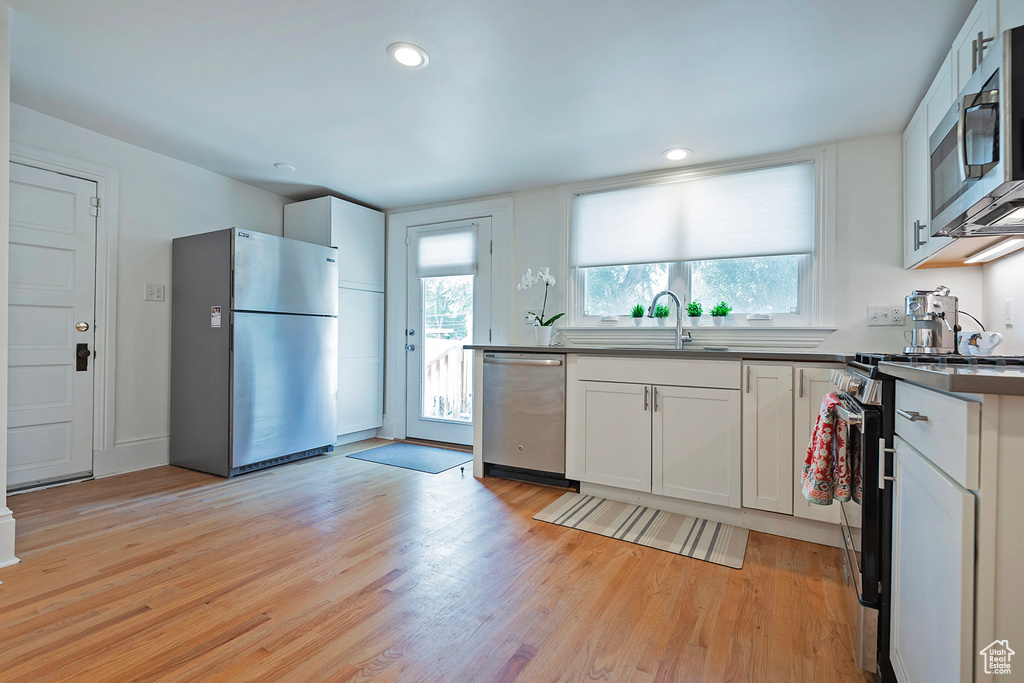 Kitchen featuring appliances with stainless steel finishes, dark countertops, light wood finished floors, white cabinetry, and recessed lighting