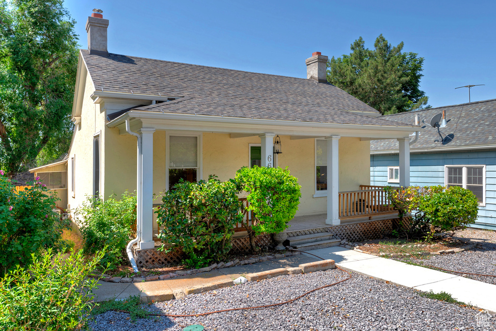 View of front of house with a chimney, covered porch, stucco siding, and a shingled roof