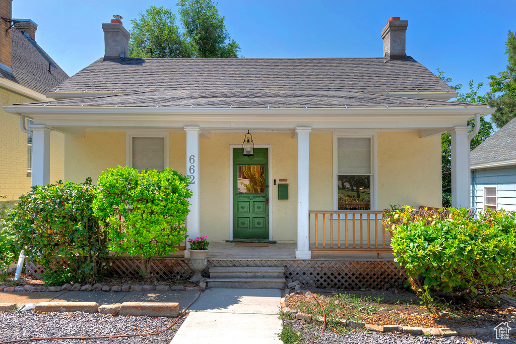 Entrance to property with a porch, a shingled roof, stucco siding, and a chimney