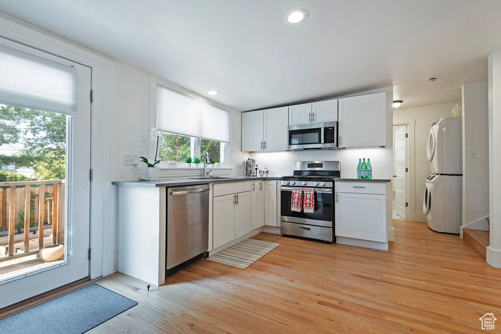 Kitchen featuring stainless steel appliances, estacked washer and dryer, white cabinets, light wood-style flooring, and recessed lighting