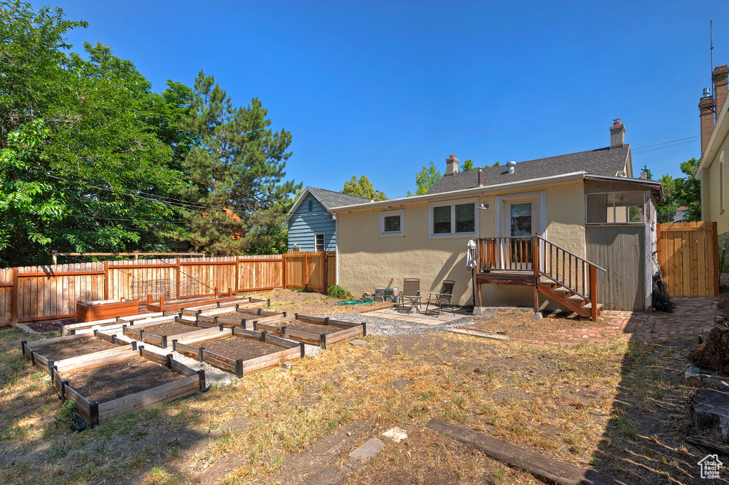 Rear view of house featuring stucco siding, a vegetable garden, and a chimney