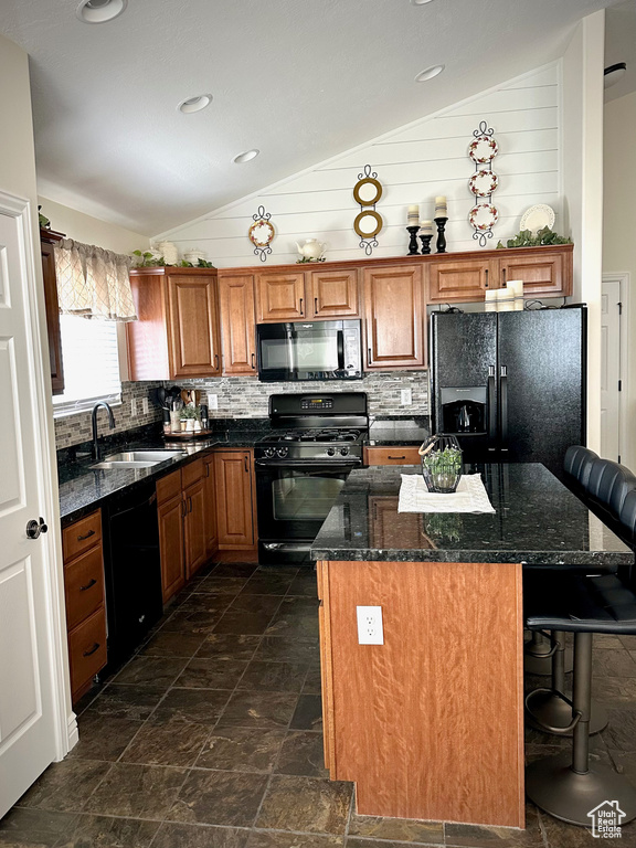 Kitchen with black appliances, vaulted ceiling, a breakfast bar area, brown cabinetry, and tasteful backsplash