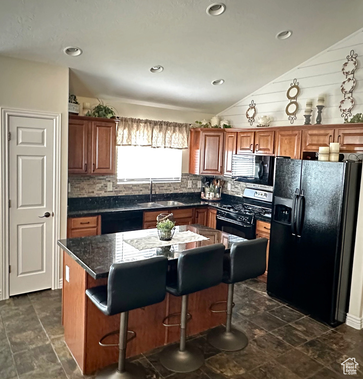Kitchen featuring black appliances, vaulted ceiling, tasteful backsplash, dark countertops, and a breakfast bar area