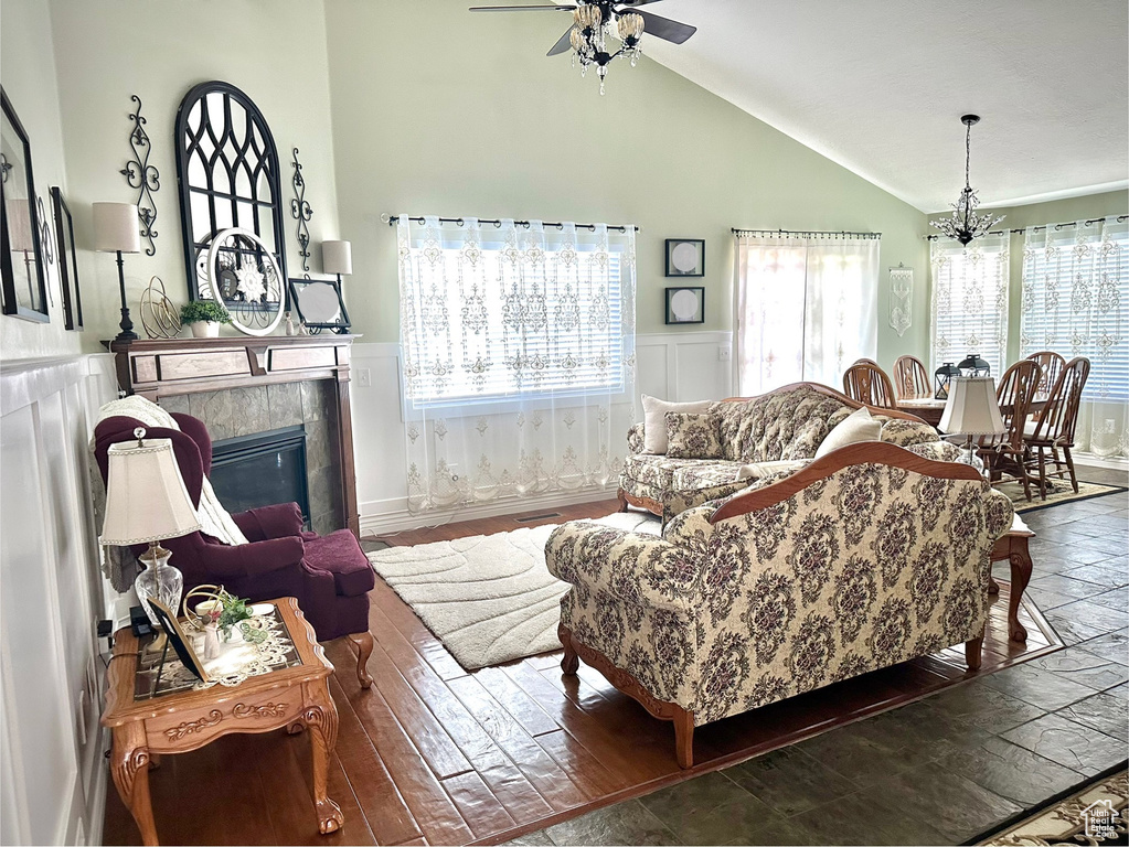 Living area featuring high vaulted ceiling, a wainscoted wall, ceiling fan, a tiled fireplace, and a chandelier
