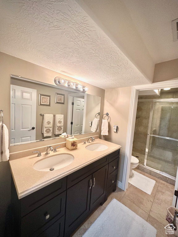 Bathroom with double vanity, a stall shower, a textured ceiling, and tile patterned flooring