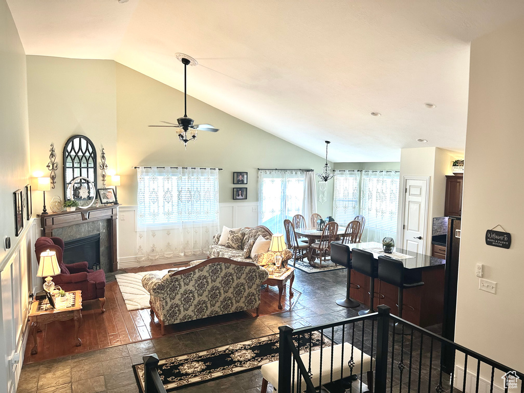 Living room featuring a tile fireplace, ceiling fan, stone tile floors, and high vaulted ceiling