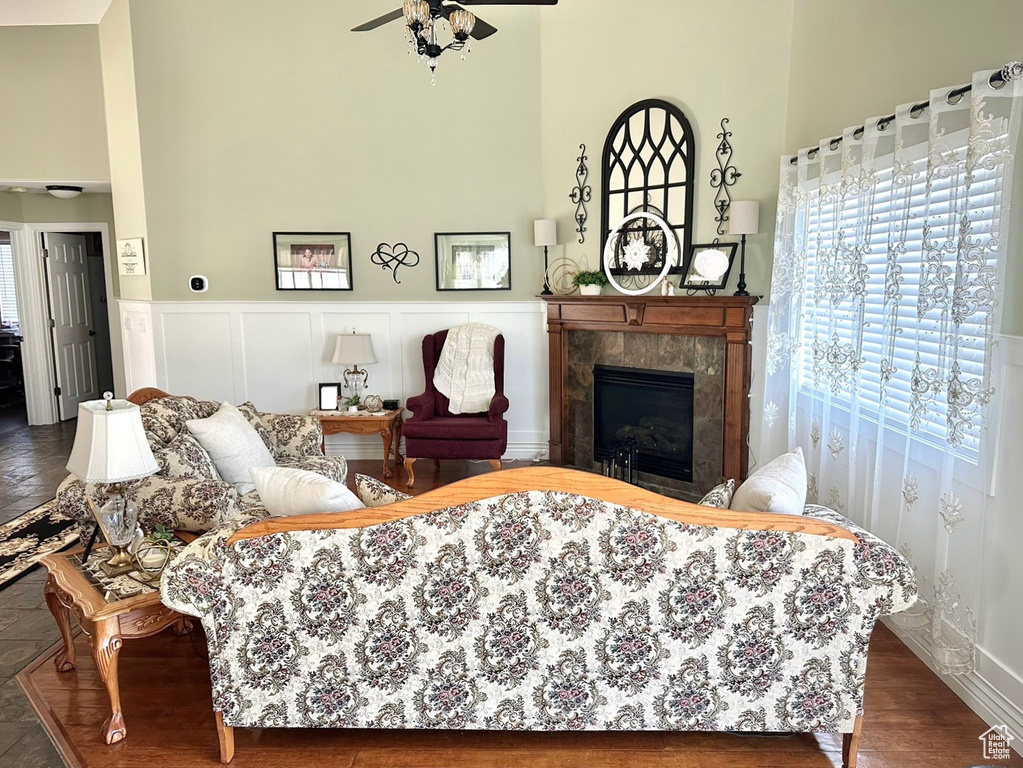 Living area featuring healthy amount of natural light, a towering ceiling, a tiled fireplace, ceiling fan, and wood finished floors