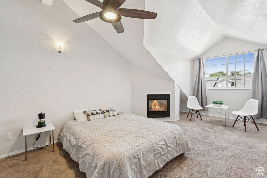 Bedroom with vaulted ceiling, carpet floors, a ceiling fan, a glass covered fireplace, and a textured ceiling