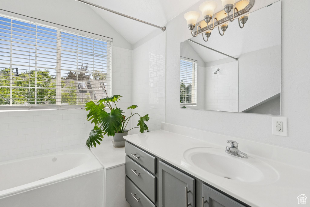 Bathroom featuring a bath, vanity, healthy amount of natural light, vaulted ceiling, and a chandelier