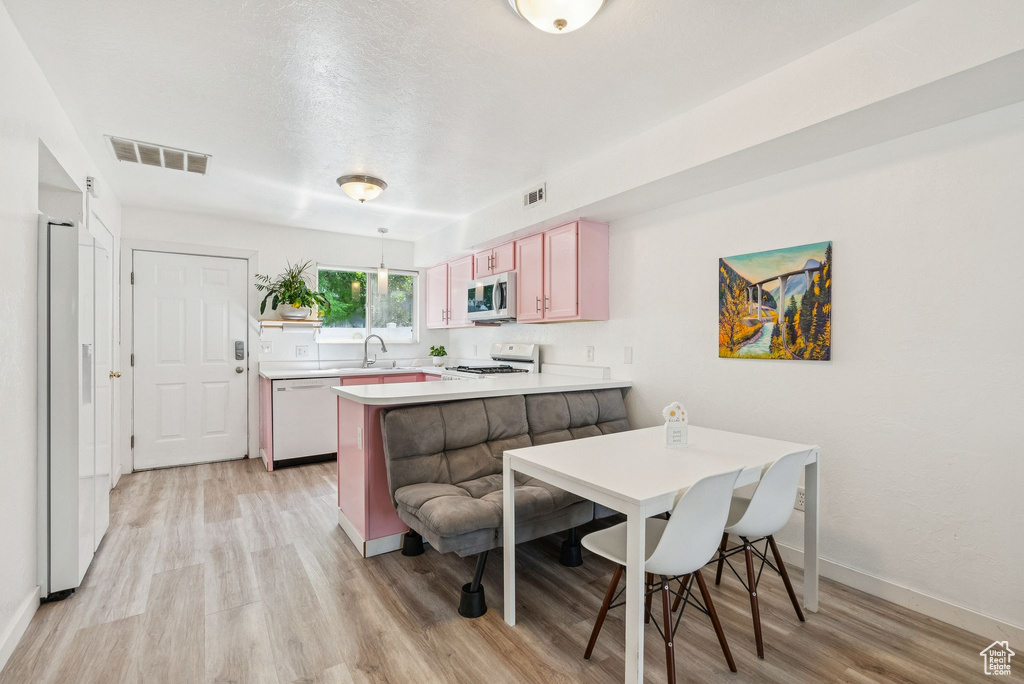 Kitchen featuring white appliances, a peninsula, light wood finished floors, and light countertops