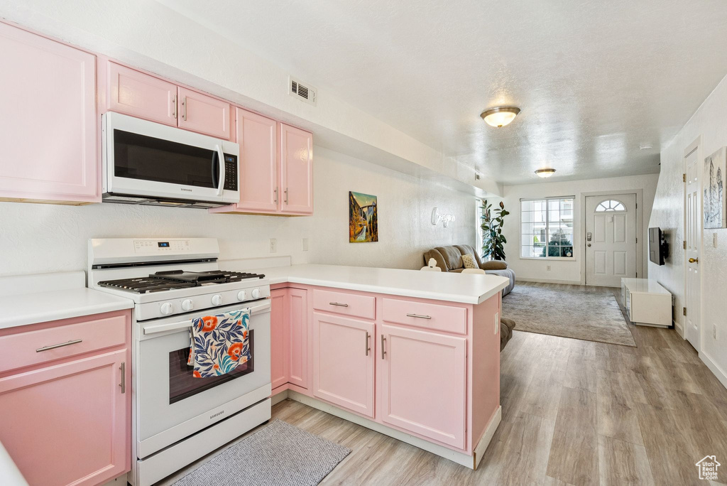 Kitchen with white appliances, open floor plan, a peninsula, light wood-style flooring, and light countertops