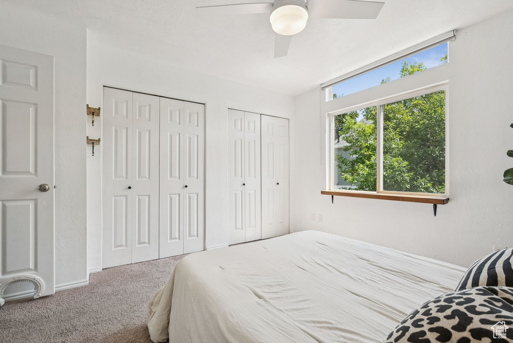 Carpeted bedroom featuring multiple closets and ceiling fan