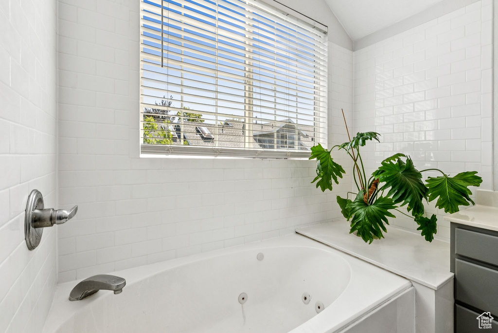 Bathroom with a jetted tub, vaulted ceiling, and vanity