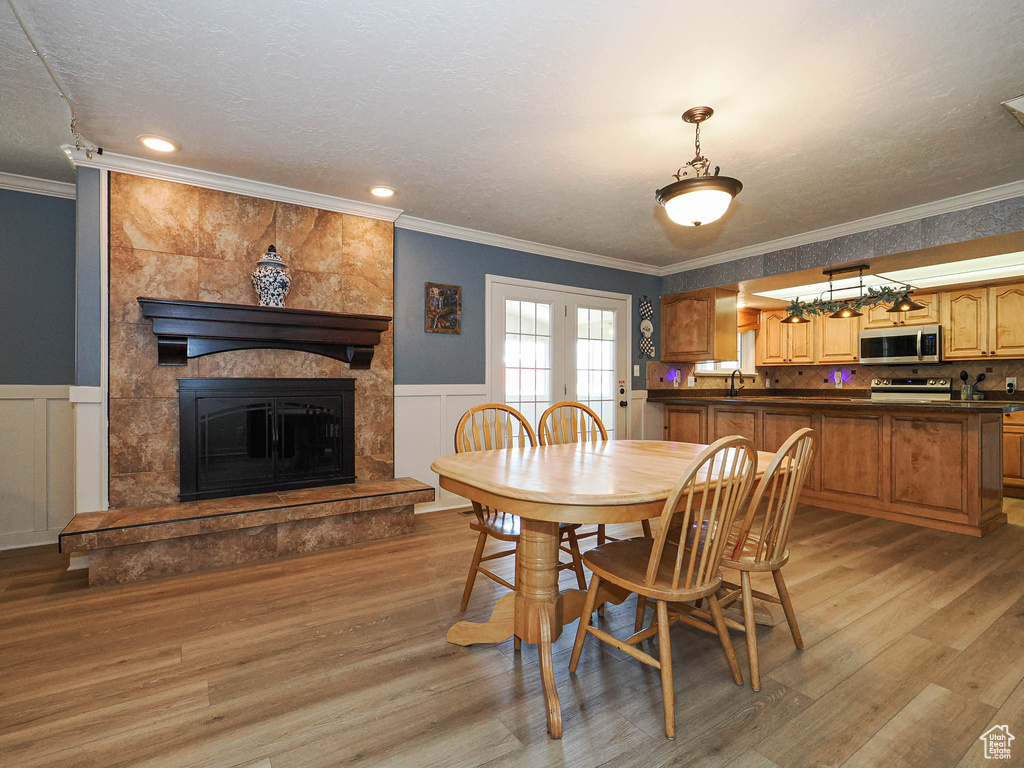 Dining space featuring light wood-style floors, a textured ceiling, ornamental molding, french doors, and a wainscoted wall