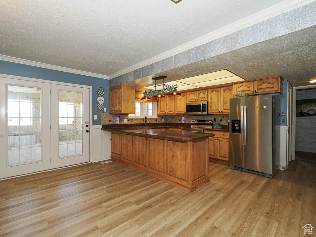 Kitchen featuring stainless steel appliances, light wood finished floors, brown cabinets, a peninsula, and a textured ceiling