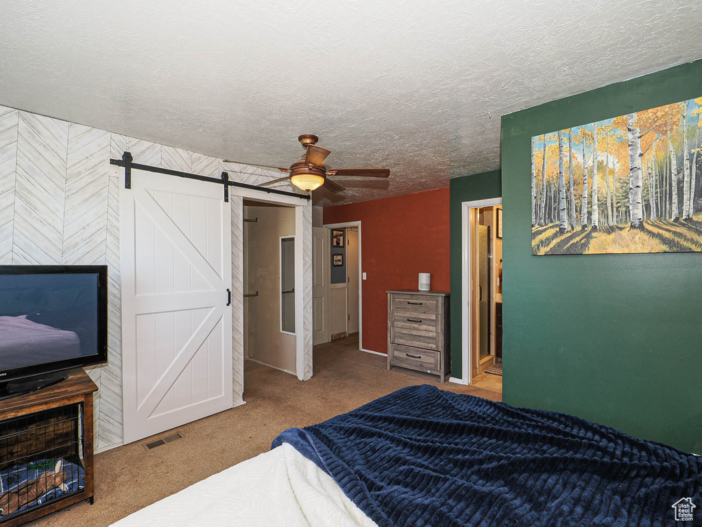 Carpeted bedroom with a barn door, a textured ceiling, and a ceiling fan