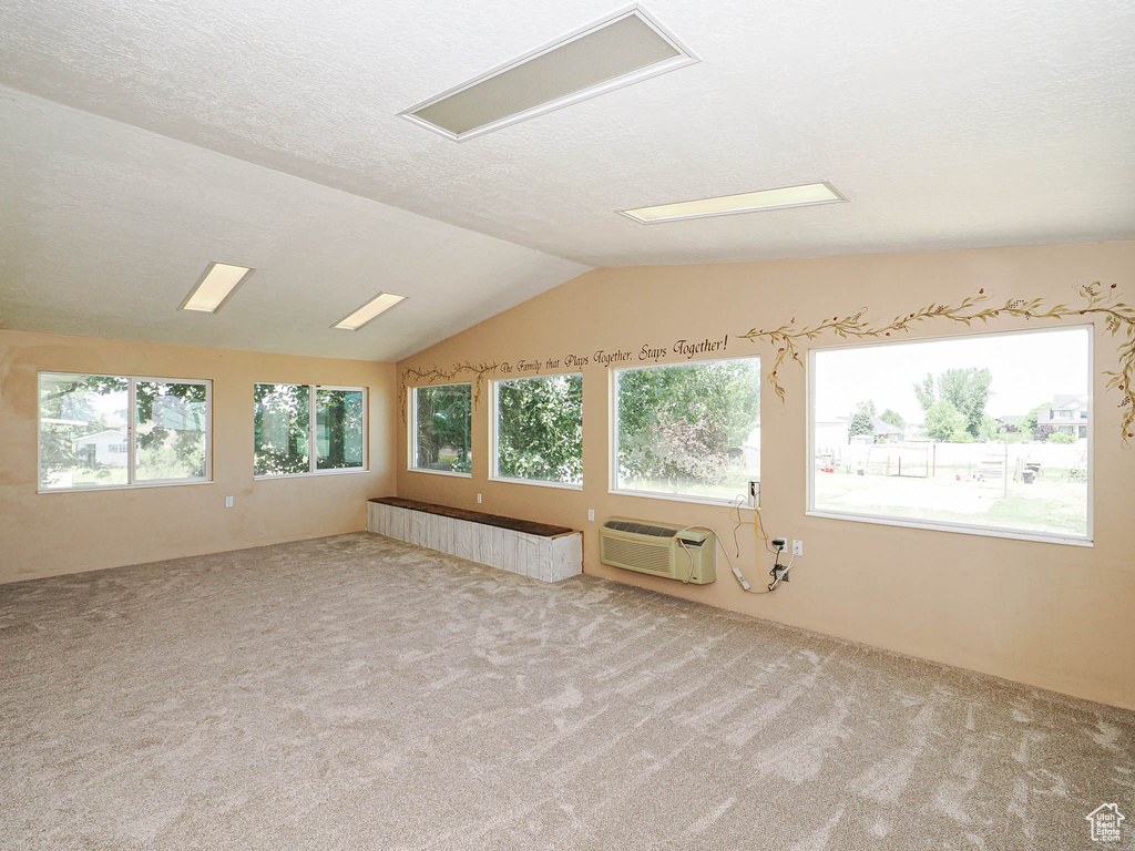 Spare room featuring carpet flooring, vaulted ceiling, a textured ceiling, and a wall unit AC
