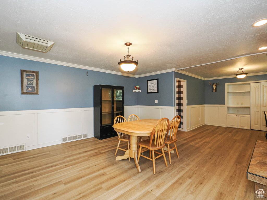 Dining area with wood finished floors, a textured ceiling, a wainscoted wall, crown molding, and a decorative wall