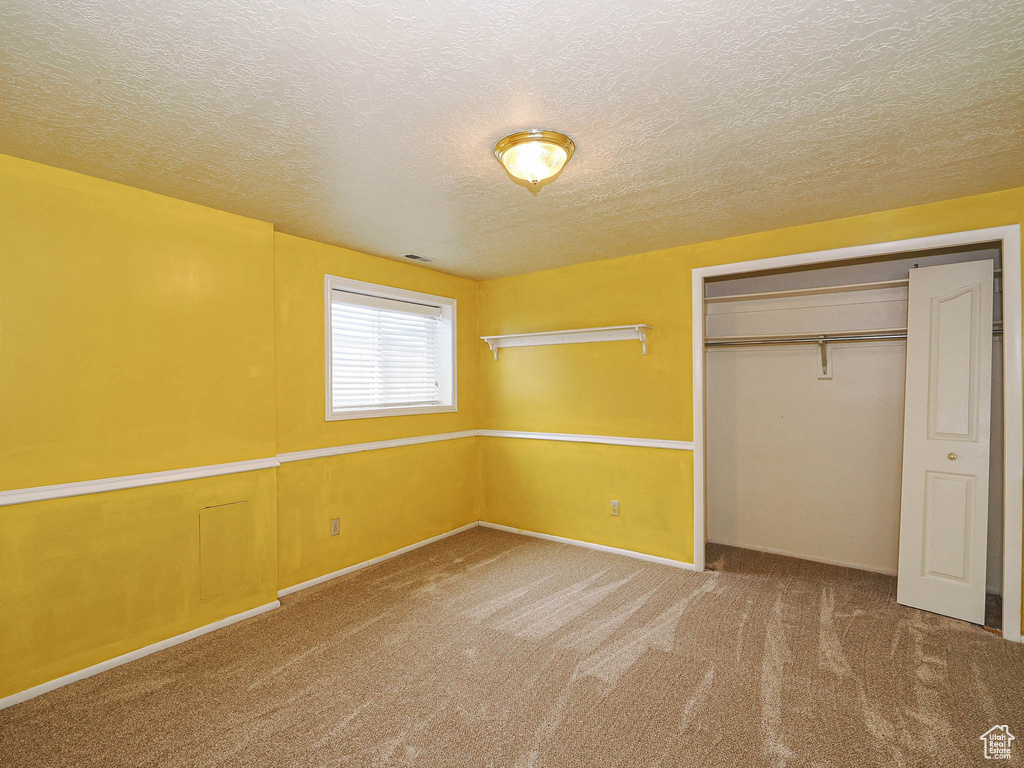 Unfurnished bedroom featuring carpet flooring, a textured ceiling, and a closet