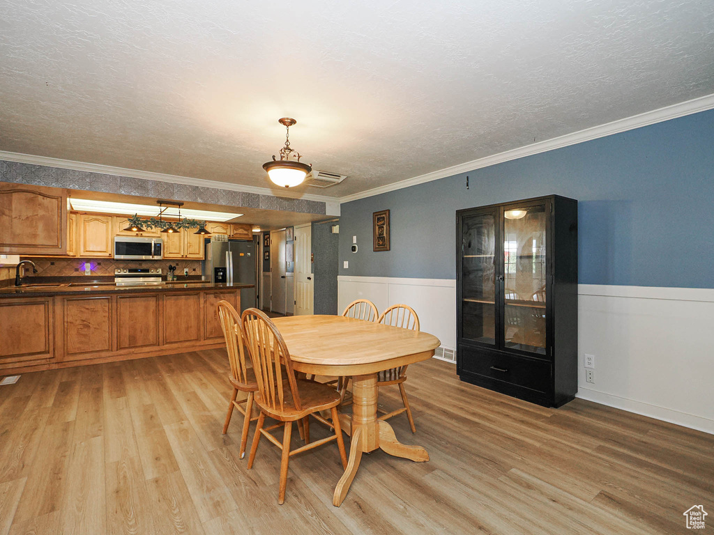 Dining area featuring light wood finished floors, crown molding, a wainscoted wall, and a textured ceiling