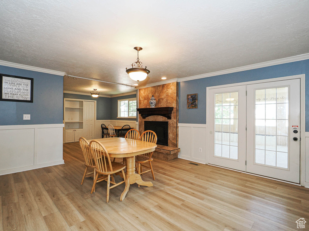 Dining space featuring light wood finished floors, a textured ceiling, a decorative wall, a wainscoted wall, and ornamental molding