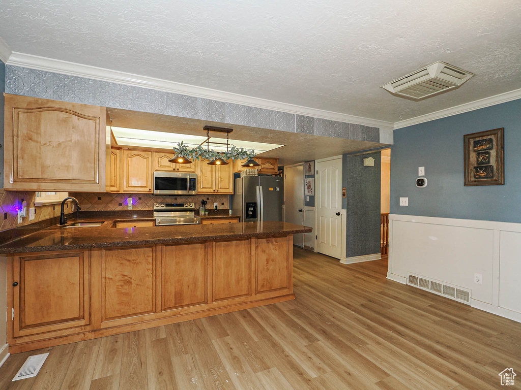 Kitchen with stainless steel appliances, ornamental molding, a peninsula, light wood finished floors, and a textured ceiling