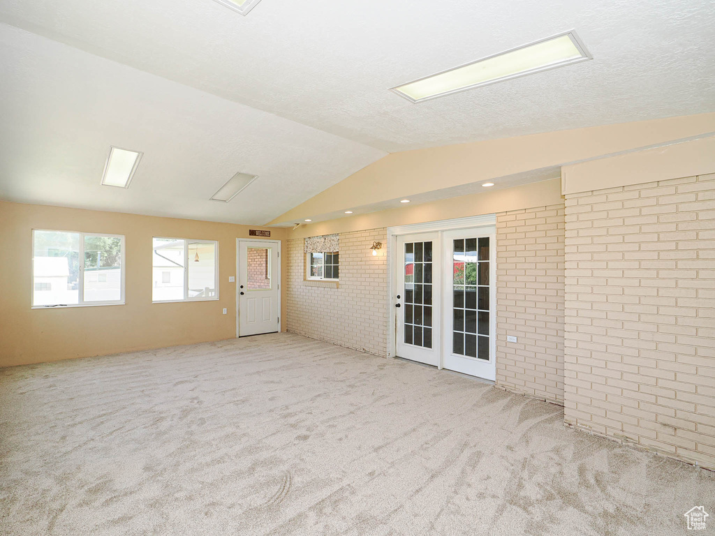 Carpeted spare room featuring brick wall, lofted ceiling, and french doors