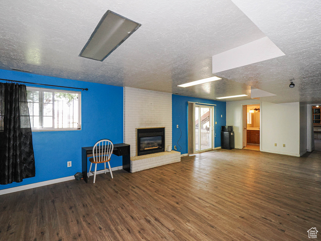 Unfurnished living room featuring a textured ceiling, wood finished floors, a brick fireplace, and plenty of natural light