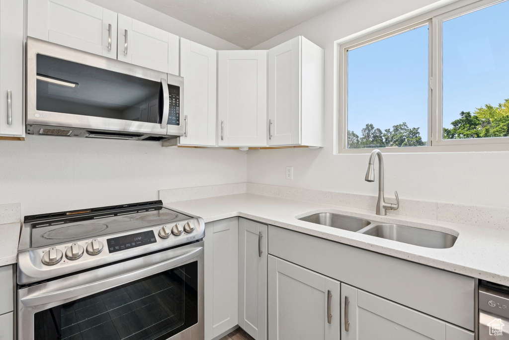Kitchen featuring stainless steel appliances, white cabinets, and light stone countertops
