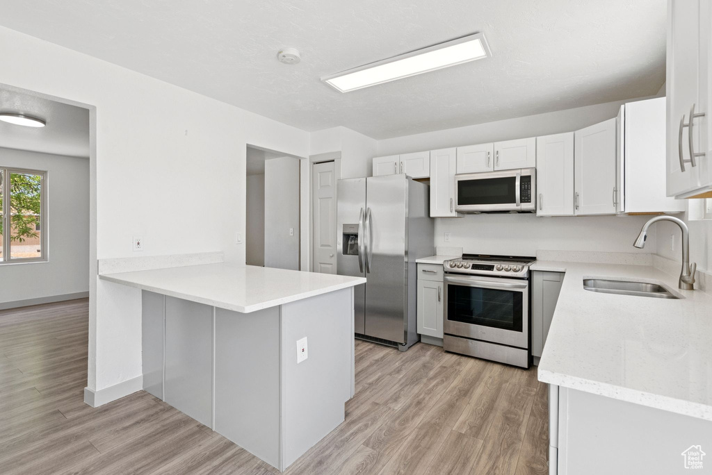 Kitchen with stainless steel appliances, a peninsula, light wood-style flooring, and light stone counters