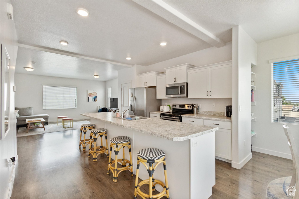 Kitchen with stainless steel appliances, a kitchen breakfast bar, wood finished floors, light countertops, and white cabinets