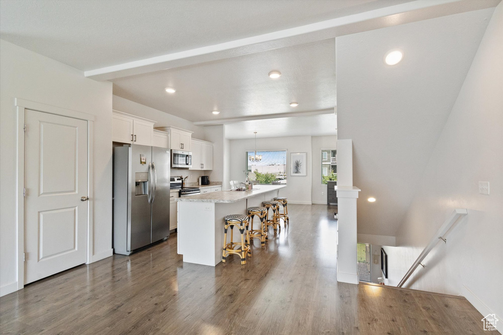 Kitchen featuring appliances with stainless steel finishes, white cabinets, a kitchen bar, dark wood finished floors, and a center island with sink