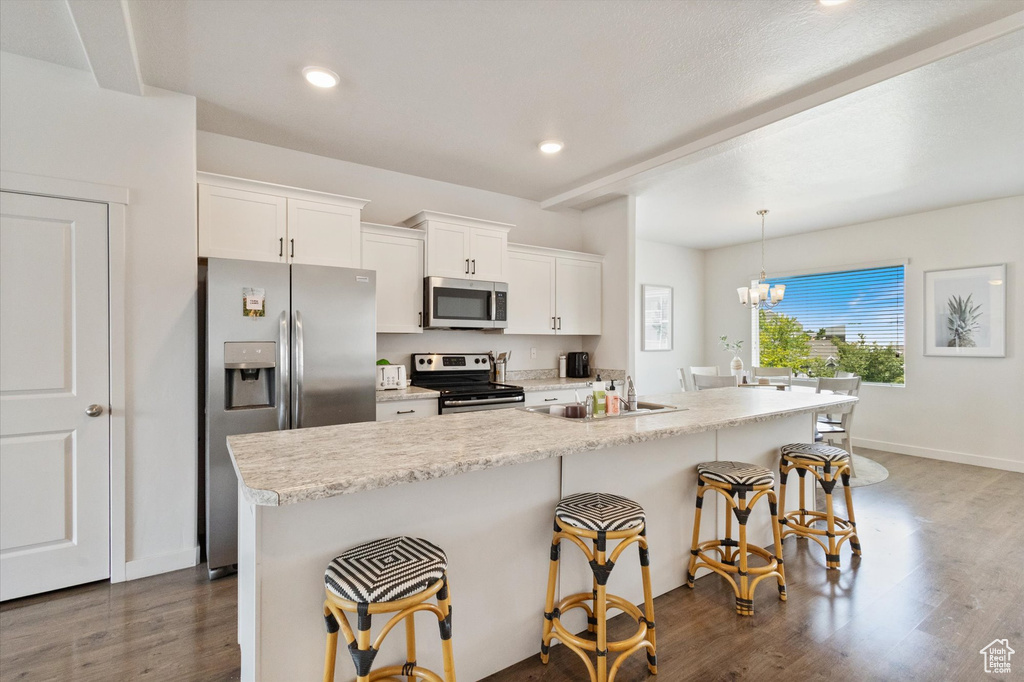 Kitchen featuring appliances with stainless steel finishes, a kitchen bar, dark wood-style flooring, an island with sink, and white cabinetry