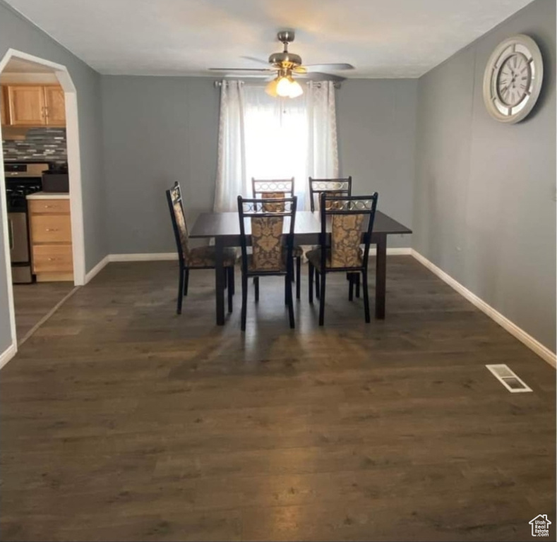 Dining space with a ceiling fan, dark wood-style flooring, and arched walkways