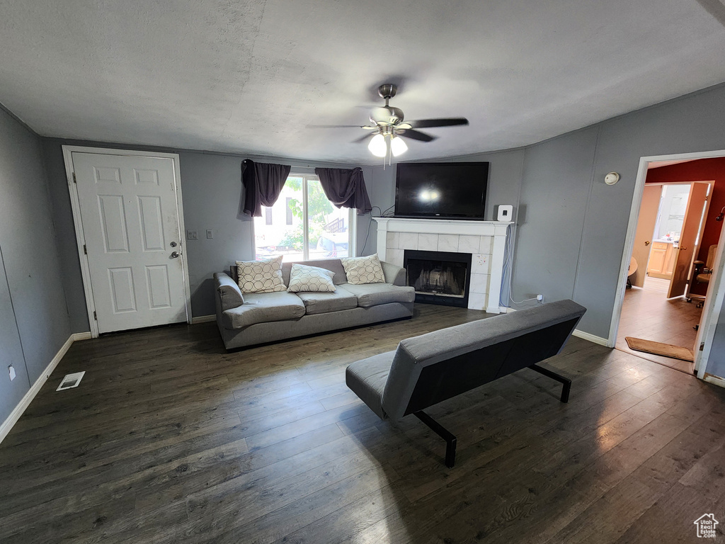 Living room featuring a ceiling fan, a fireplace, and dark wood-style flooring