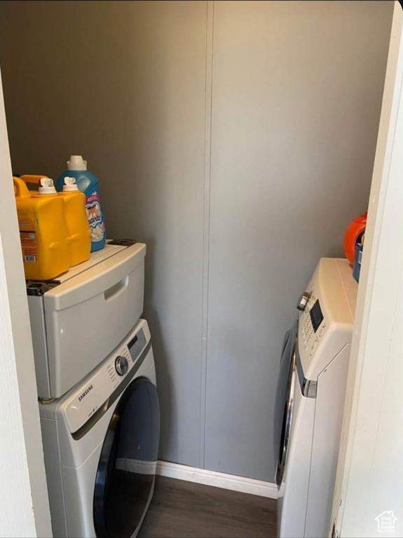 Laundry area with stacked washer / drying machine and wood finished floors