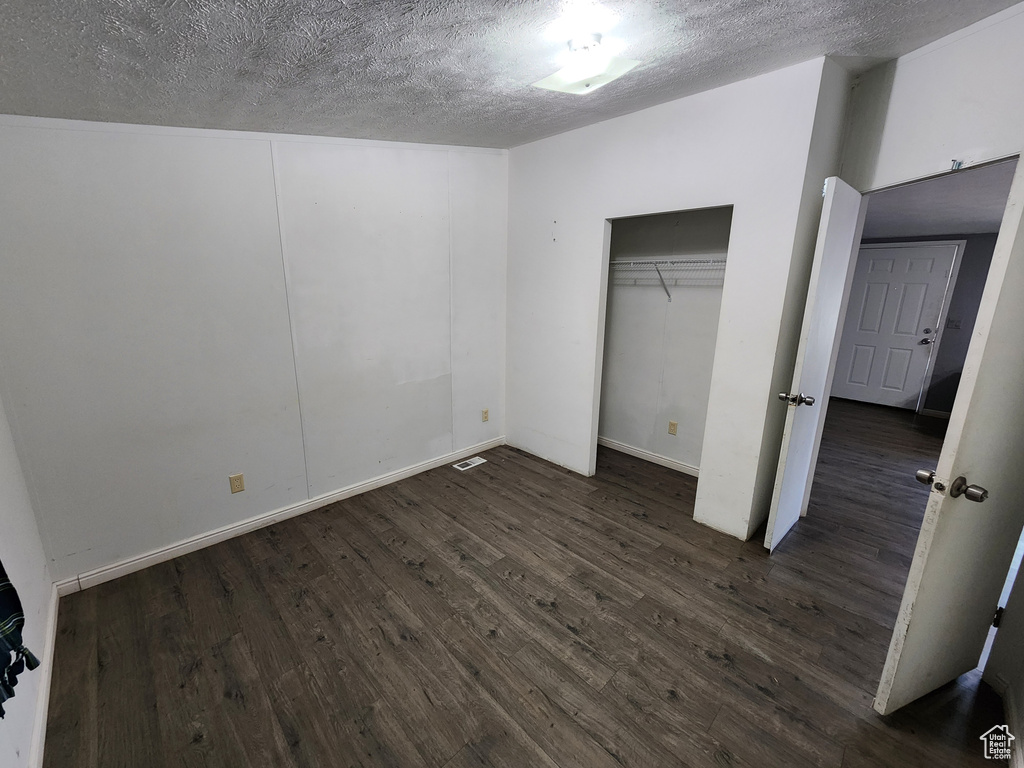 Unfurnished bedroom with dark wood-style floors, a textured ceiling, and a closet