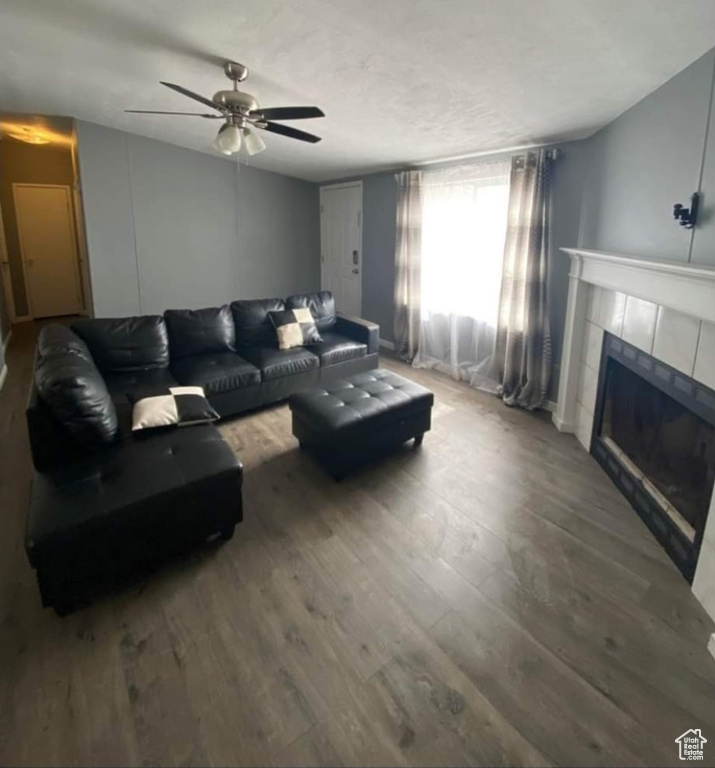 Living room with a ceiling fan, a tile fireplace, and wood finished floors