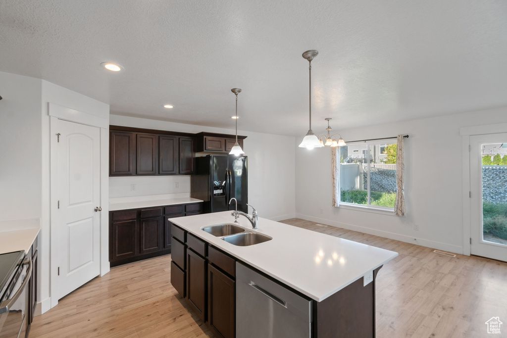 Kitchen with appliances with stainless steel finishes, light wood finished floors, a chandelier, light countertops, and dark brown cabinets