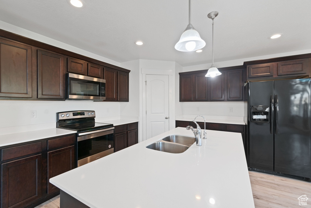 Kitchen with appliances with stainless steel finishes, recessed lighting, dark brown cabinets, decorative light fixtures, and light wood-style flooring