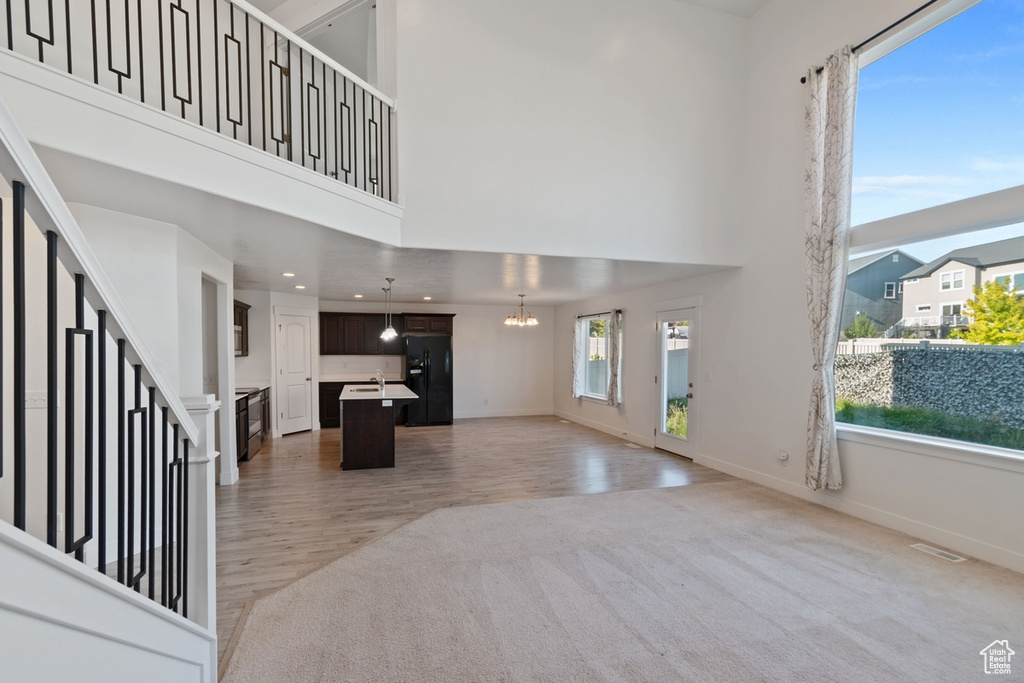 Unfurnished living room featuring light colored carpet, a chandelier, a towering ceiling, recessed lighting, and light wood-style floors