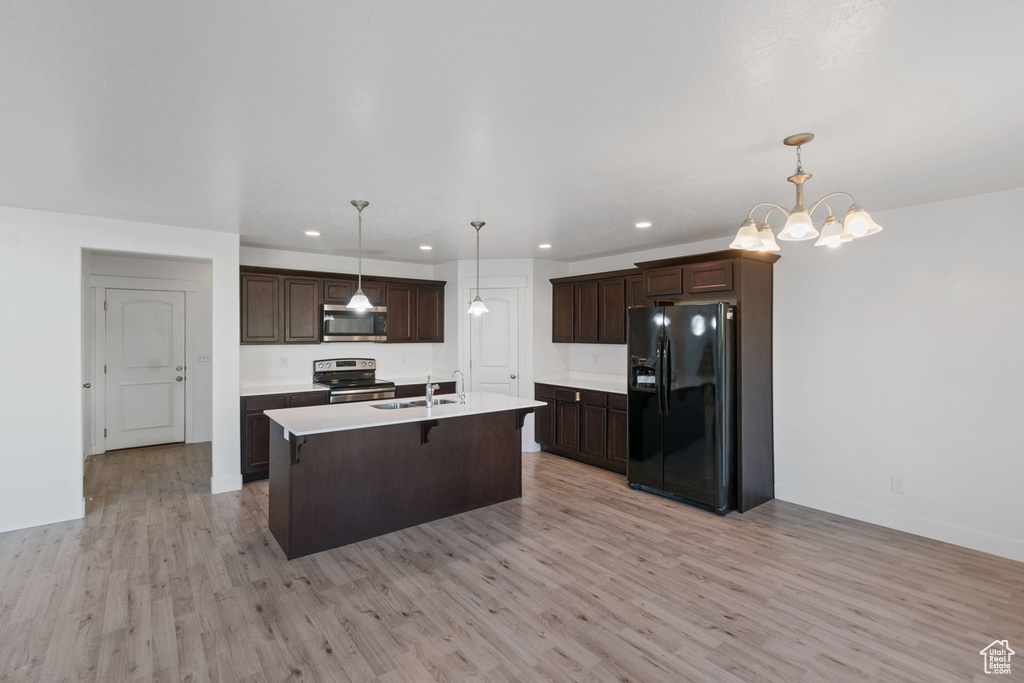 Kitchen featuring stainless steel appliances, light wood-style floors, dark brown cabinets, light countertops, and a kitchen island with sink