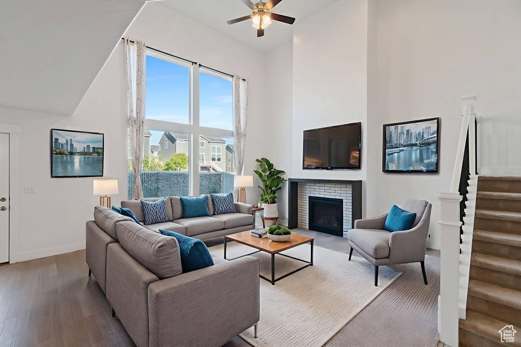 Living area featuring high vaulted ceiling, ceiling fan, wood finished floors, stairway, and a brick fireplace